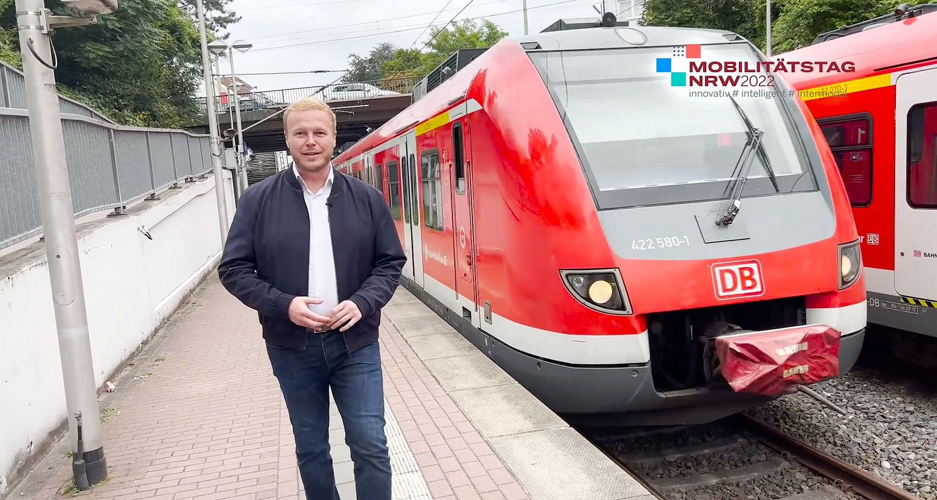 Moderator Tobias Häusler läuft an einem Bahnsteig vor einem roten Zug vorbei.